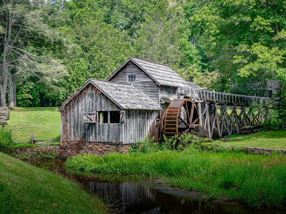 Old mill beside a still pond surrounded by turning autumn trees